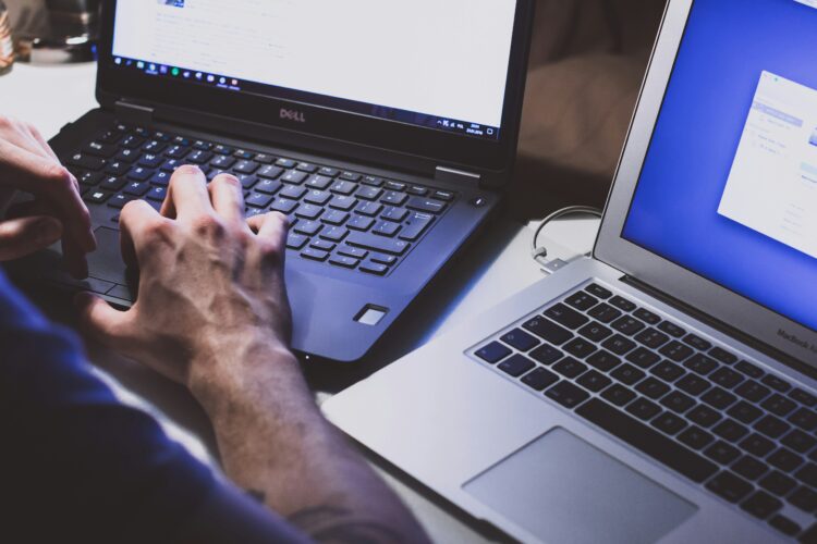 two laptops side by side and a person typing in one