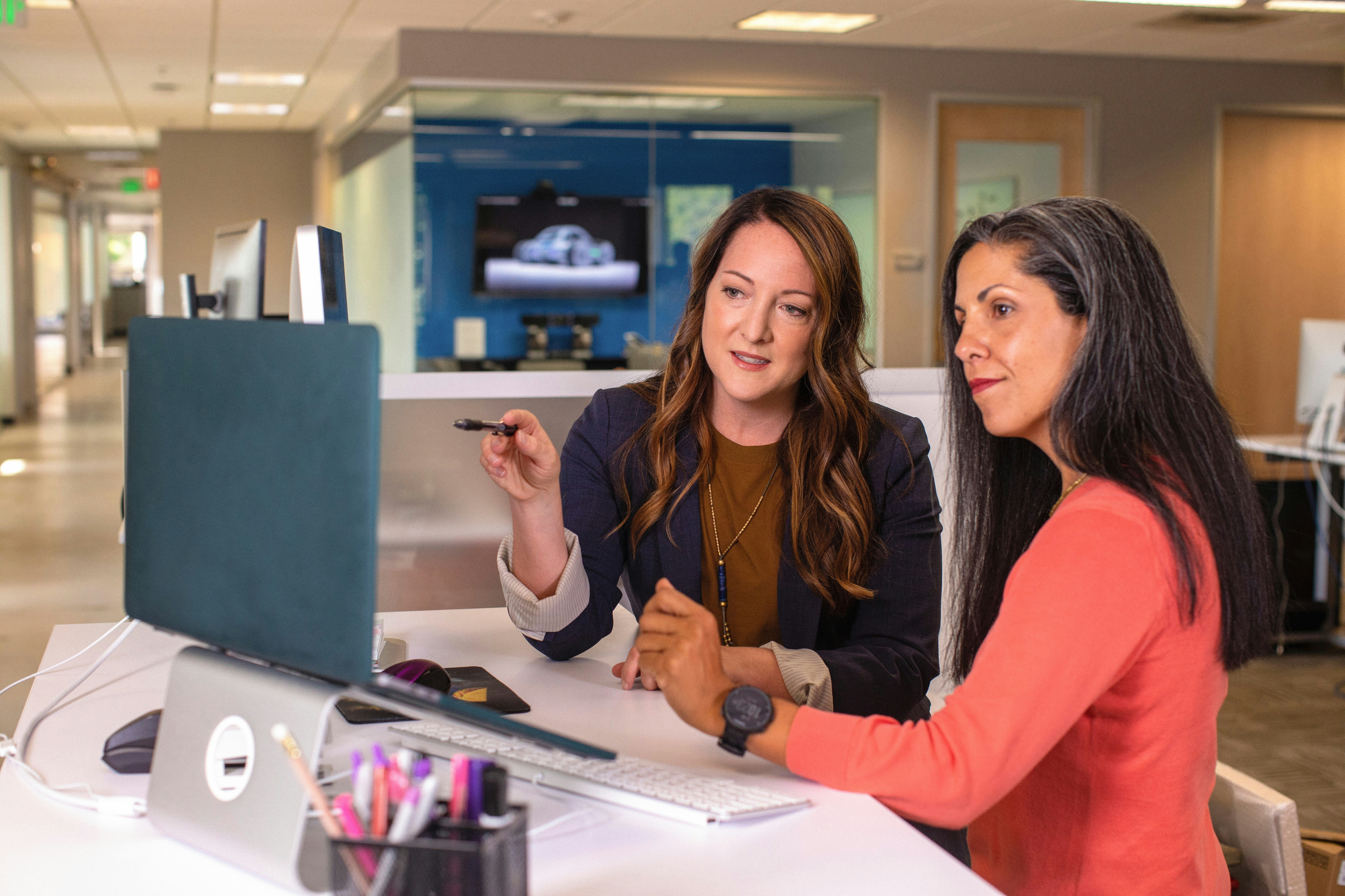Two women discussing marketing data on a desktop computer in a modern office. - AI Marketing Tools Two women discussing marketing data on a desktop computer in a modern office.
