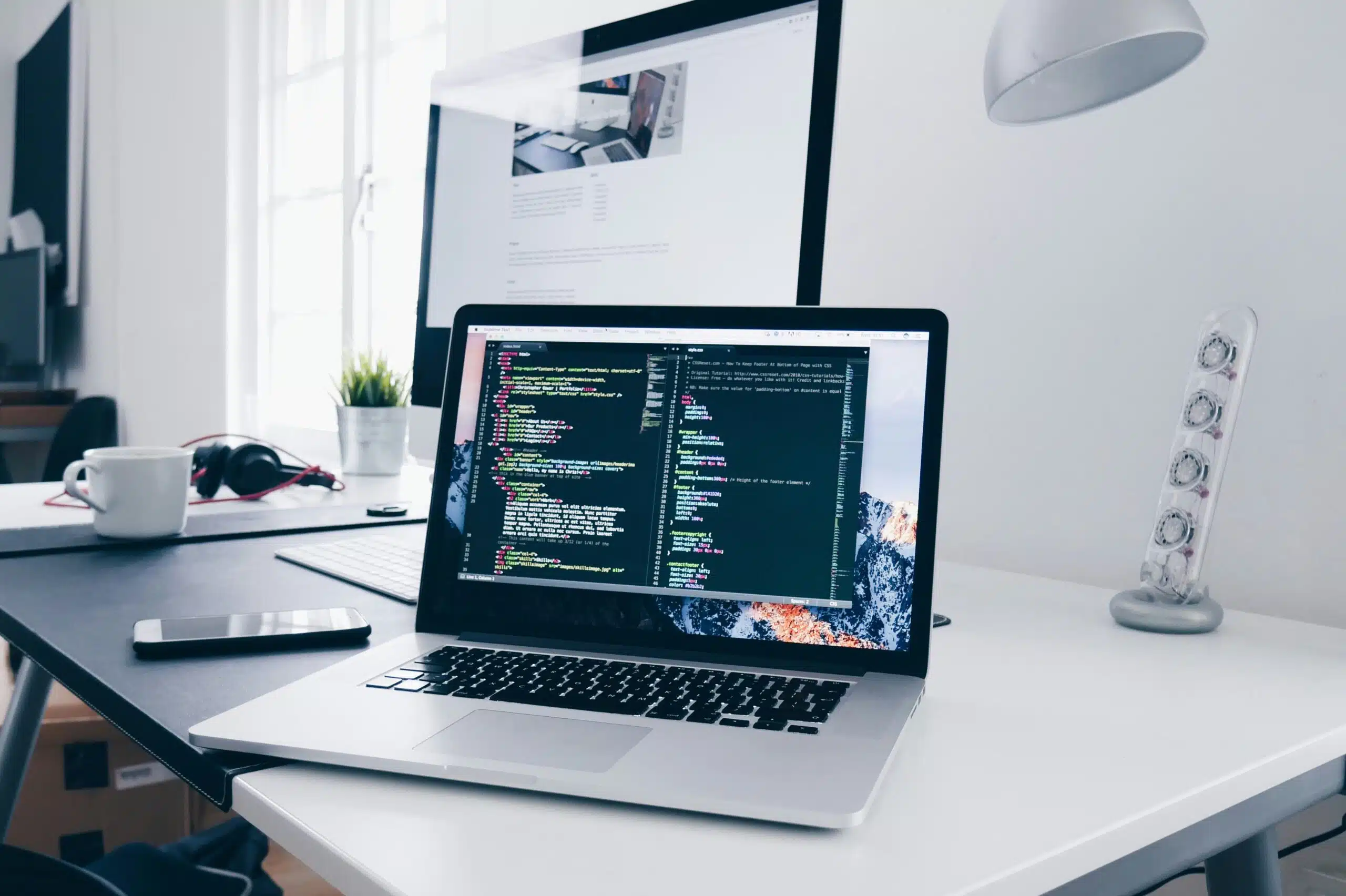Laptop displaying code on a desk with a larger screen in the background, representing AI copywriting tool comparison.