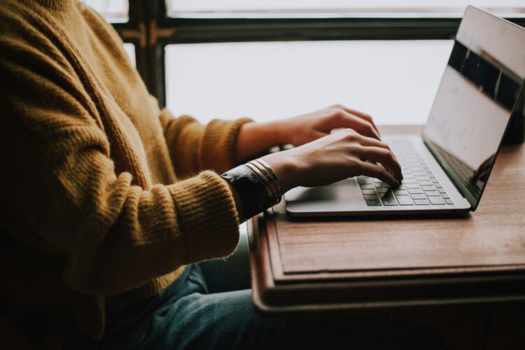 Person typing on a laptop near a window