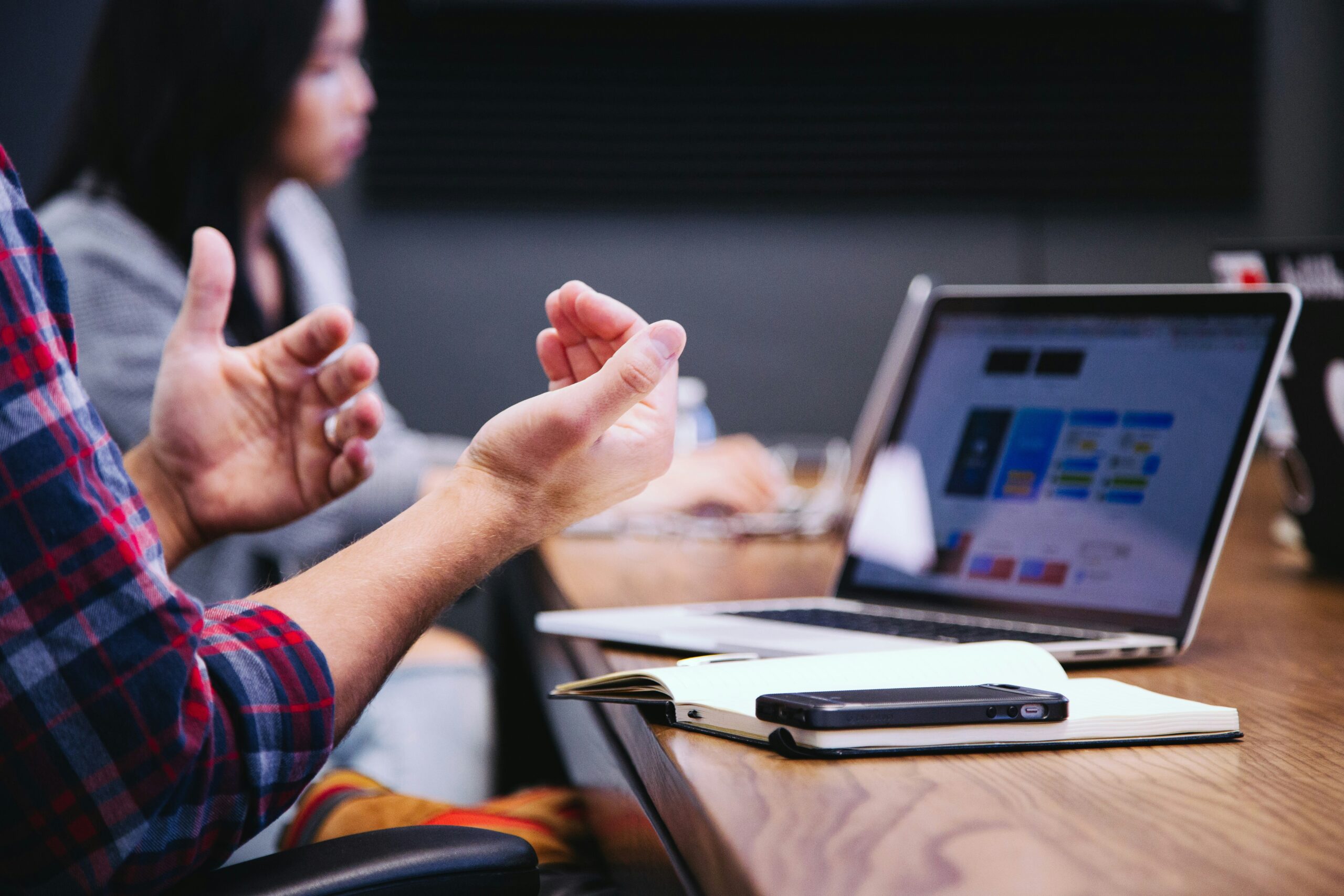 A person gesturing during a discussion, with a laptop screen displaying SEO-related content