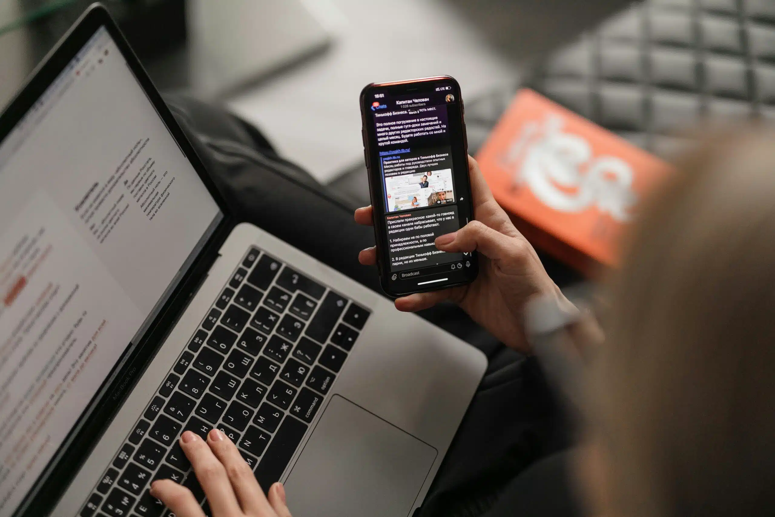 a person working on laptop while also scrolling social media on phone