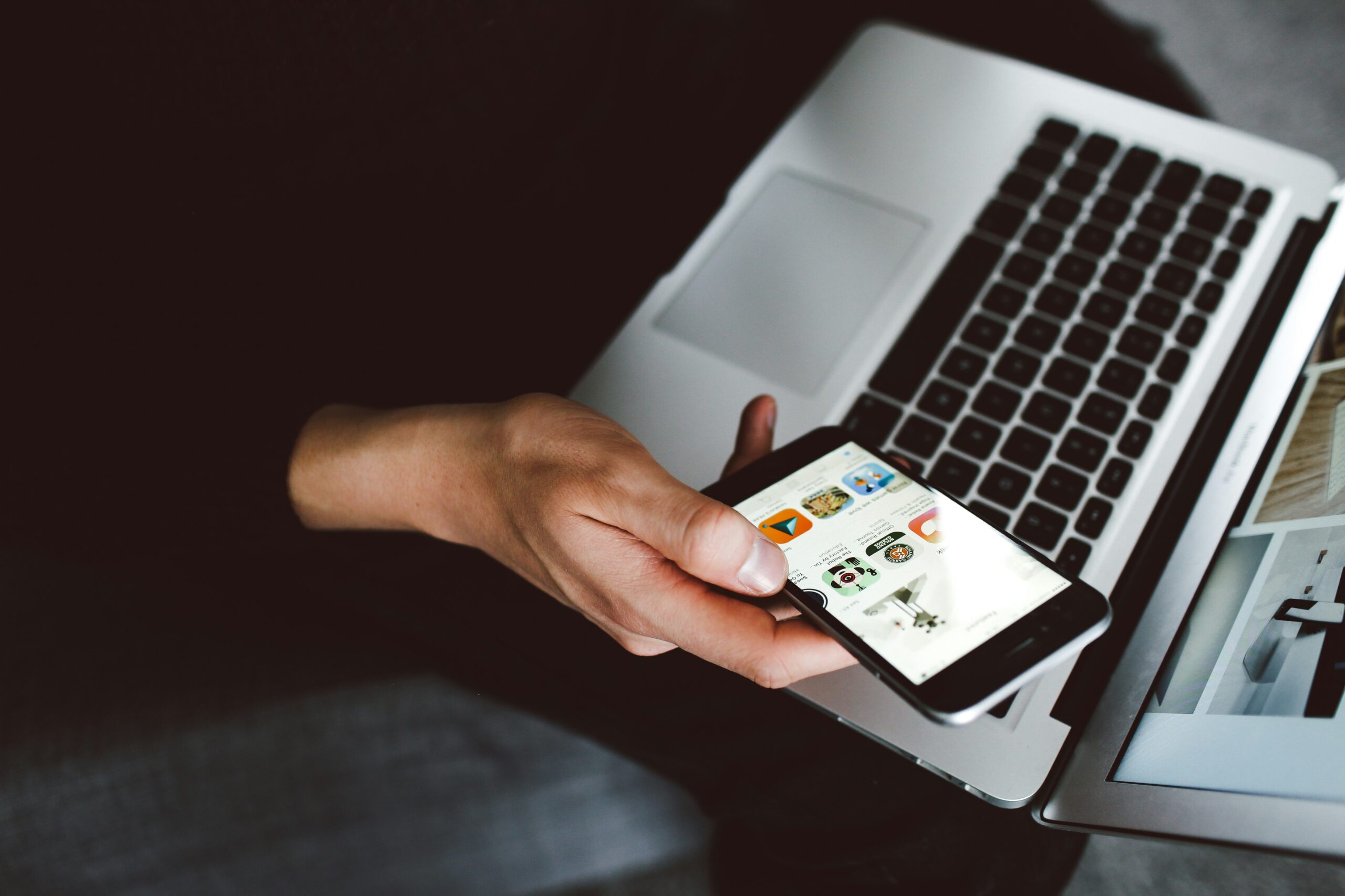 A person holding a smartphone while using a laptop