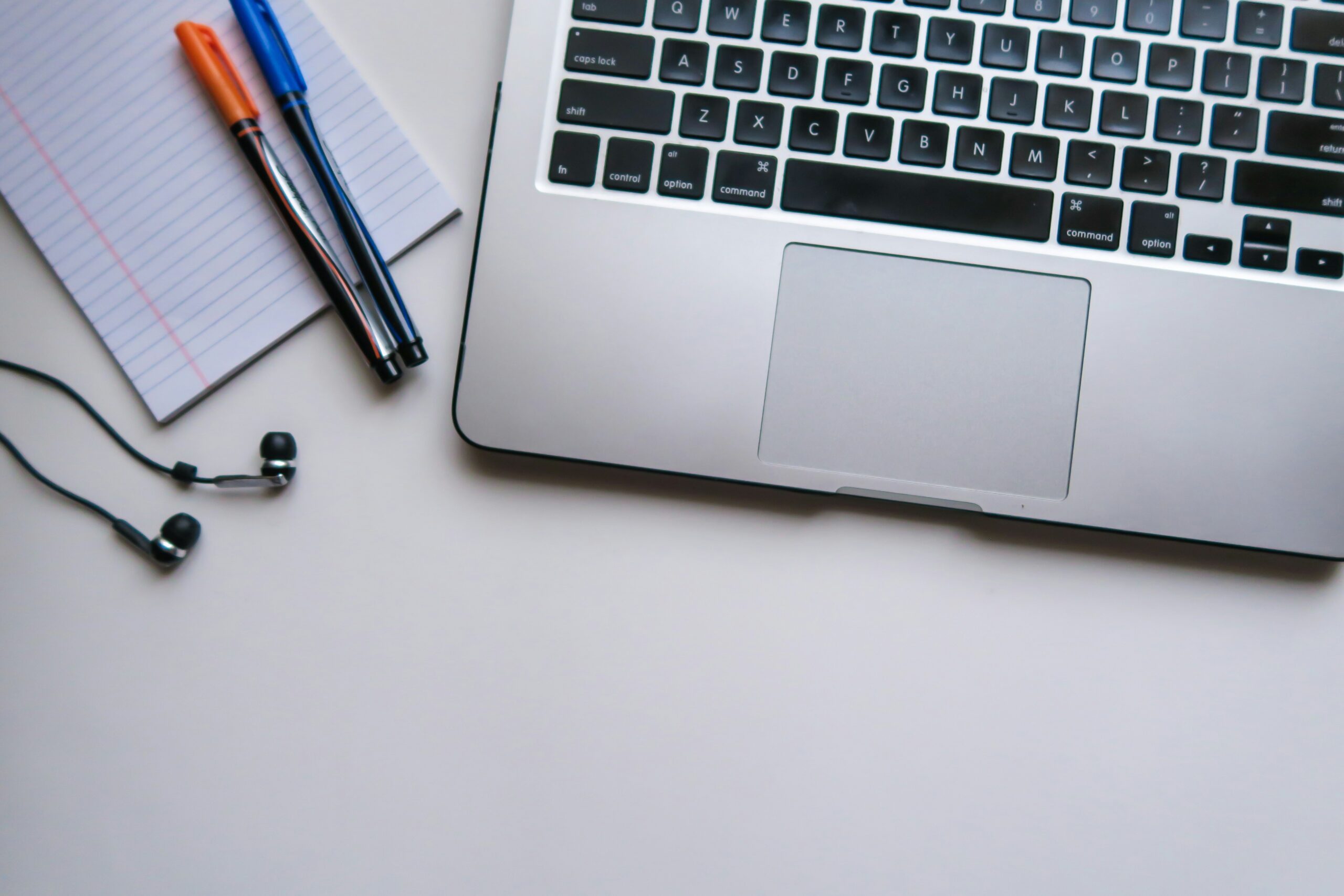 a laptop with notebook and pens on a desk