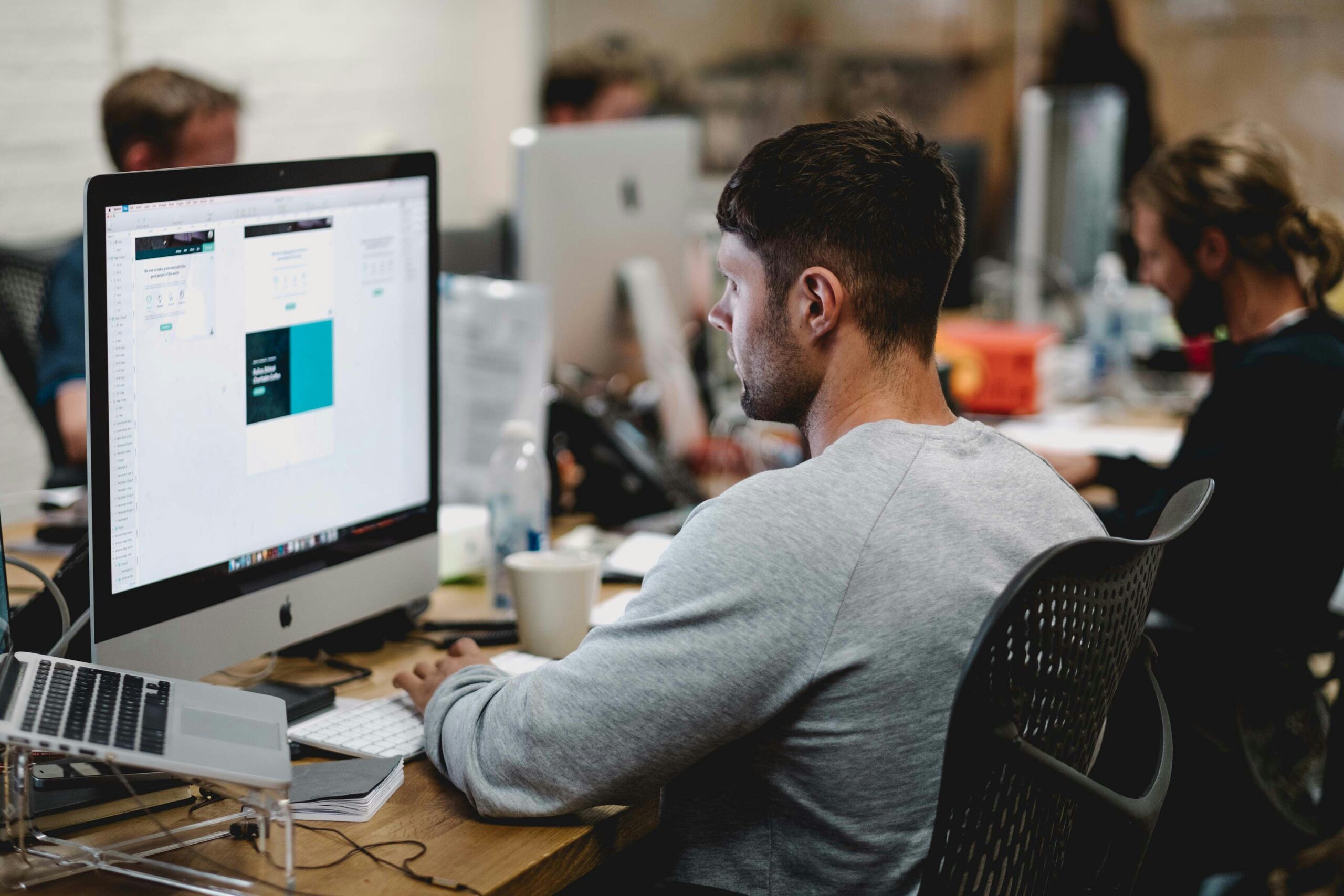 A focused professional using AI software on a desktop in a dynamic office setting.