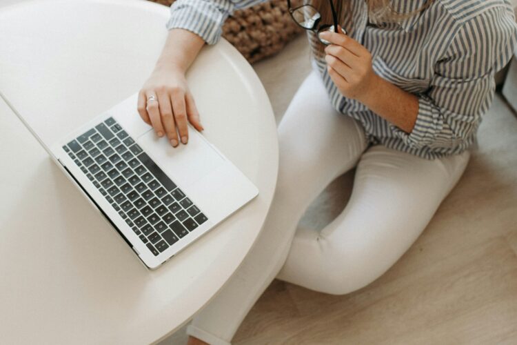 Woman sitting on the floor, holding glasses and engaged in content marketing on her laptop.