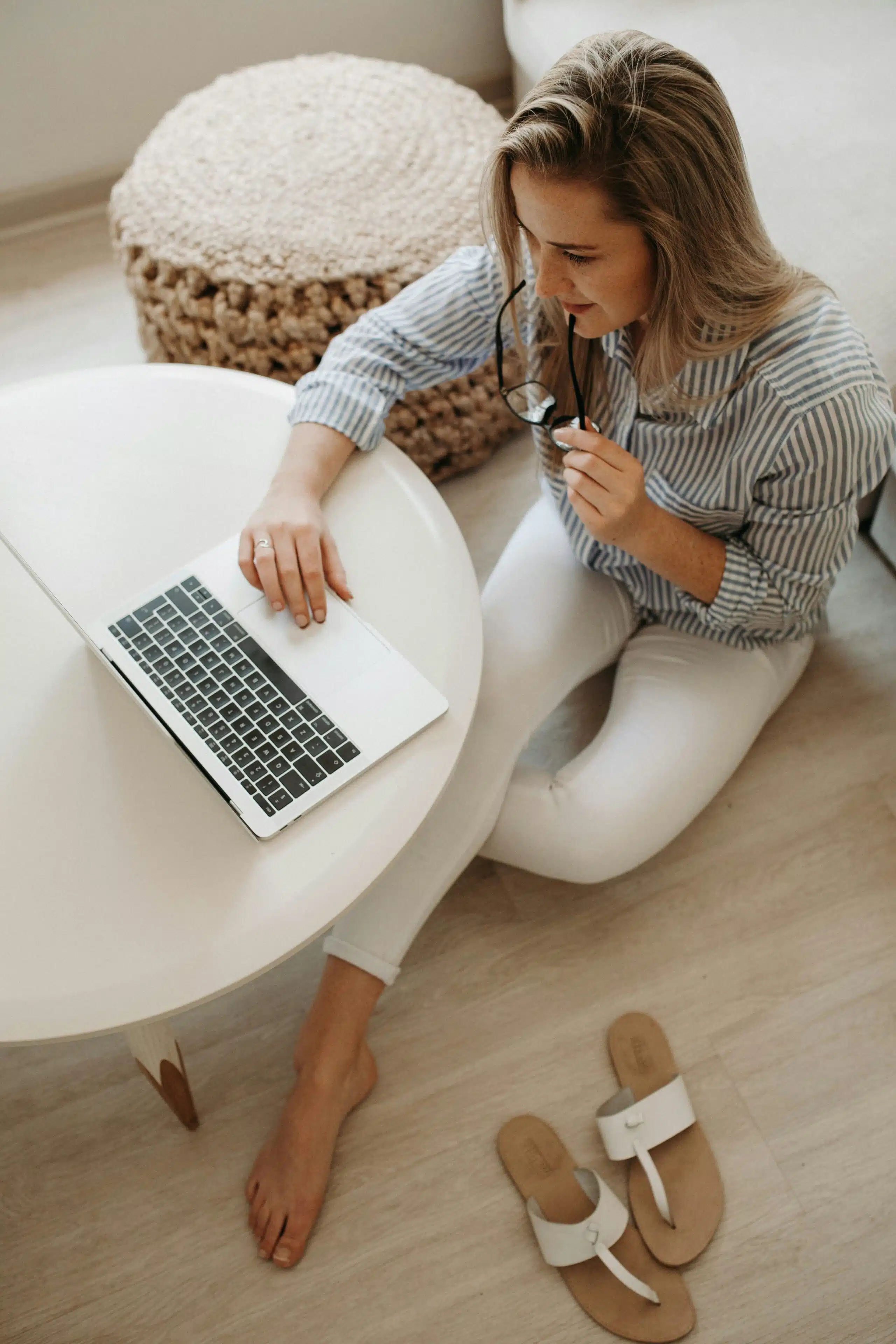 Woman sitting on the floor, holding glasses and engaged in content marketing on her laptop.