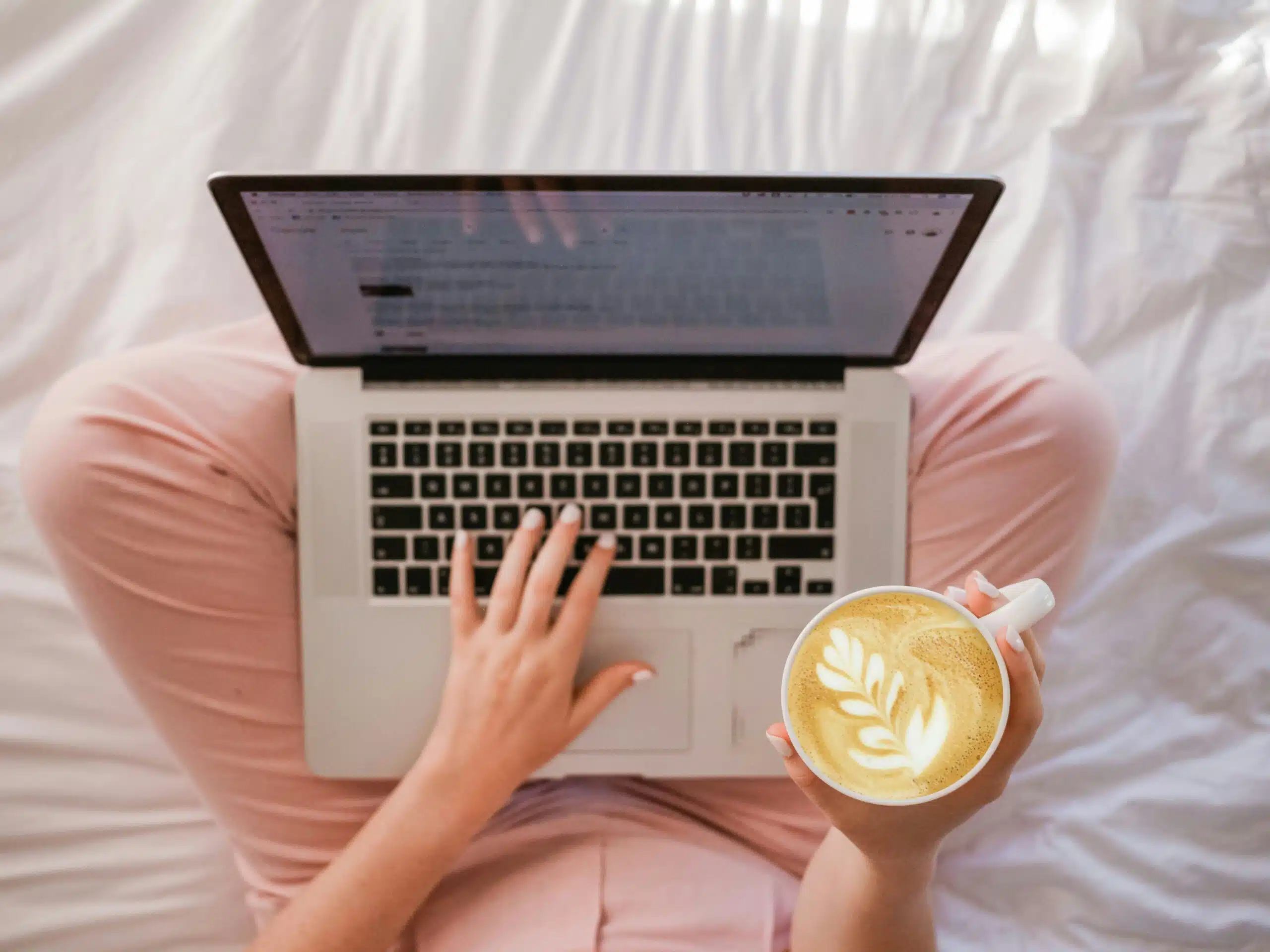 Person using a laptop while holding a latte, depicting the ease of AI-assisted content generation.