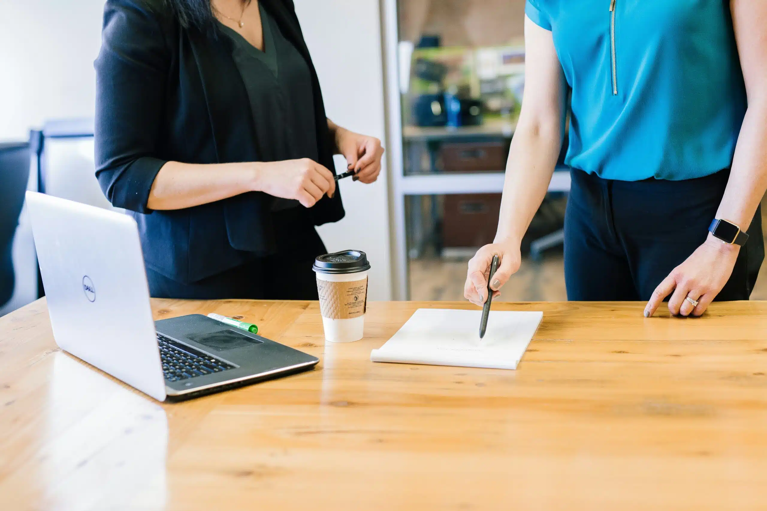 Two businesswomen in discussion over a report, with a laptop on the table
