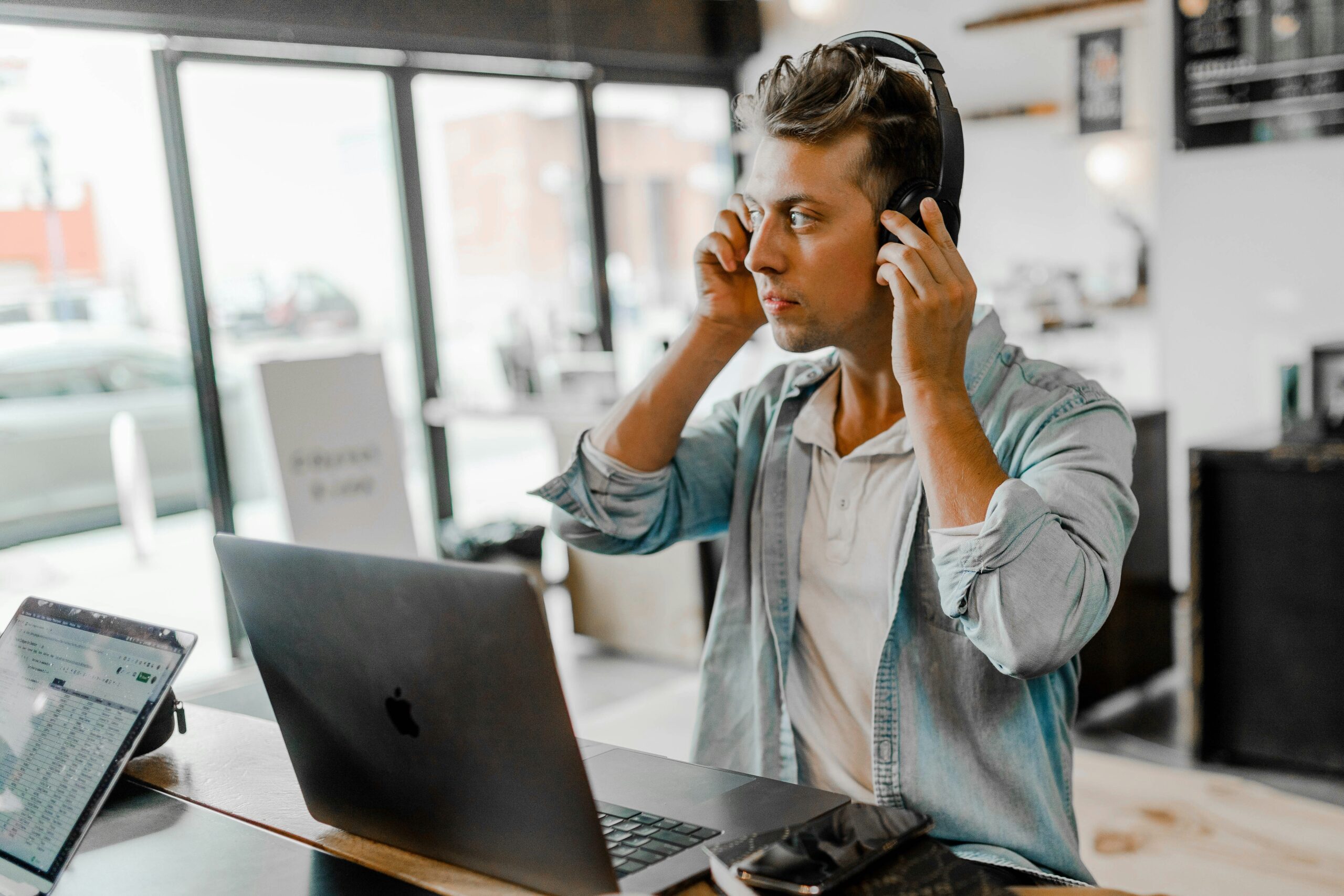 A man in a café using a laptop and wearing headphones.