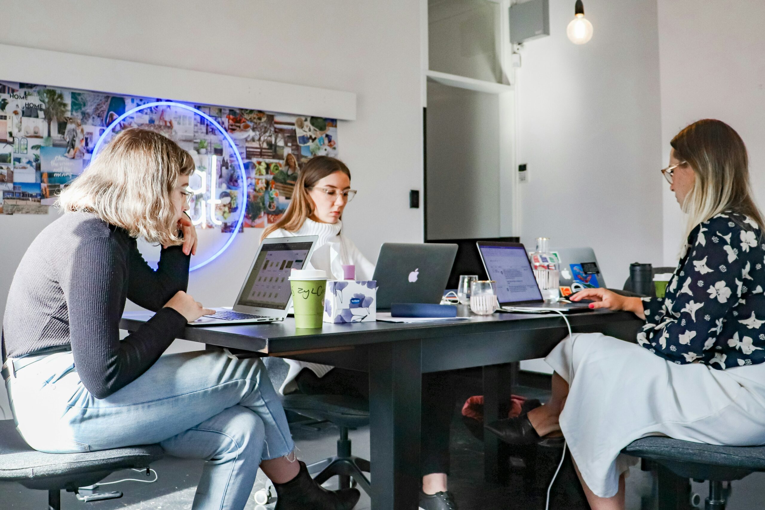 Three women in a meeting room, working on laptops and discussing content optimization approaches.