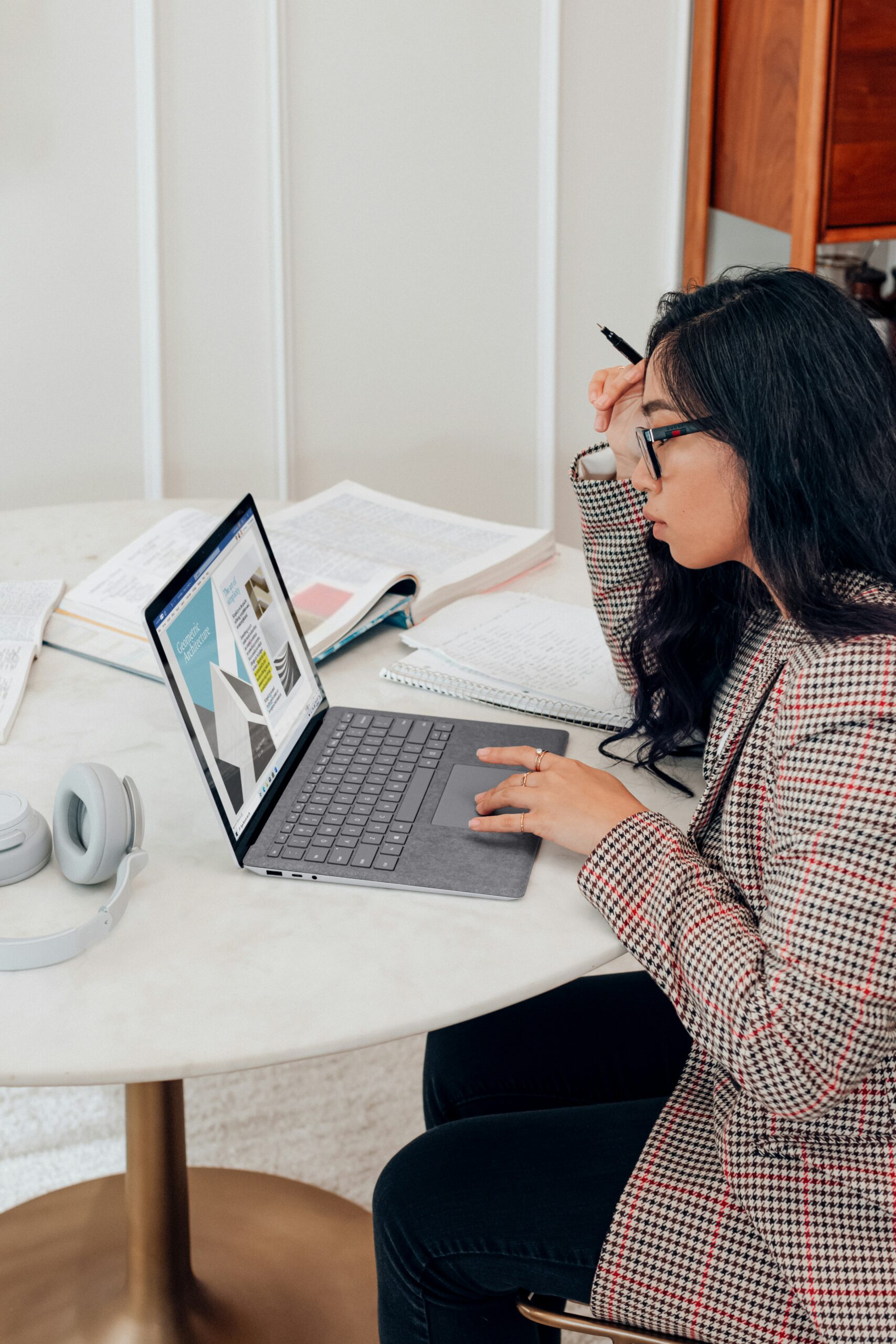 Woman analyzing content on a laptop, surrounded by notes and books