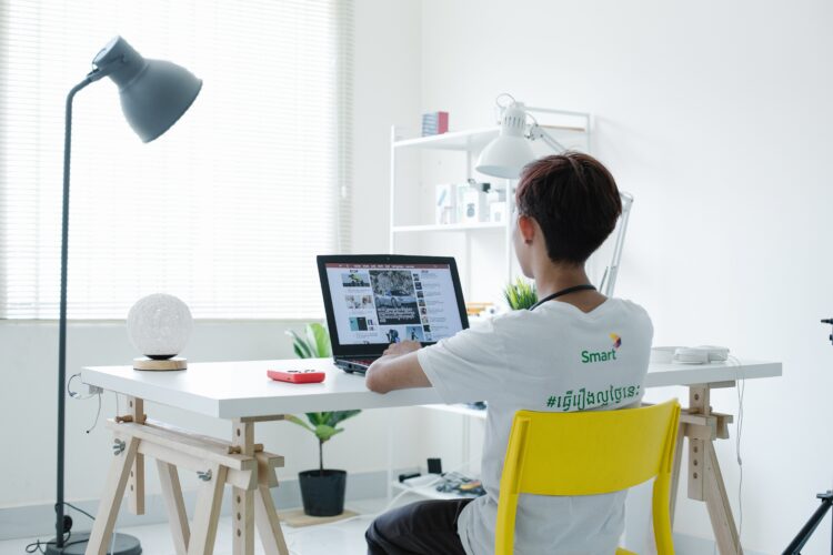 Person sitting at a white desk in a modern, minimalistic room, researching on a laptop.