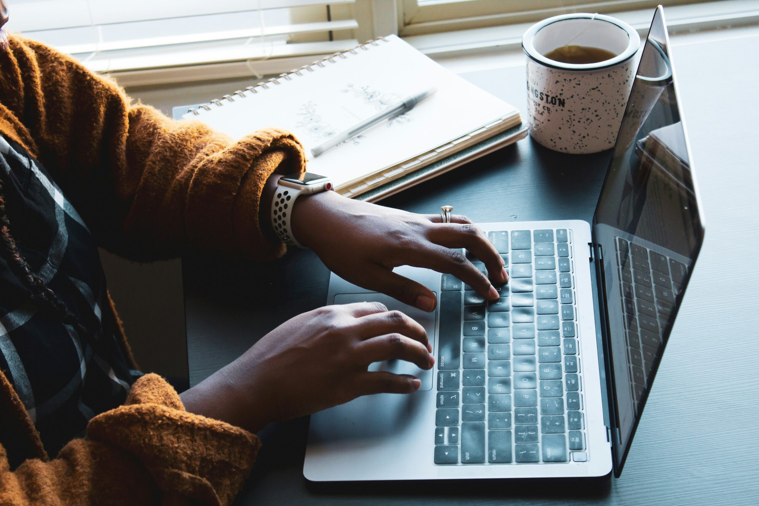  Woman's Hands typing on a laptop near a notebook and coffee cup