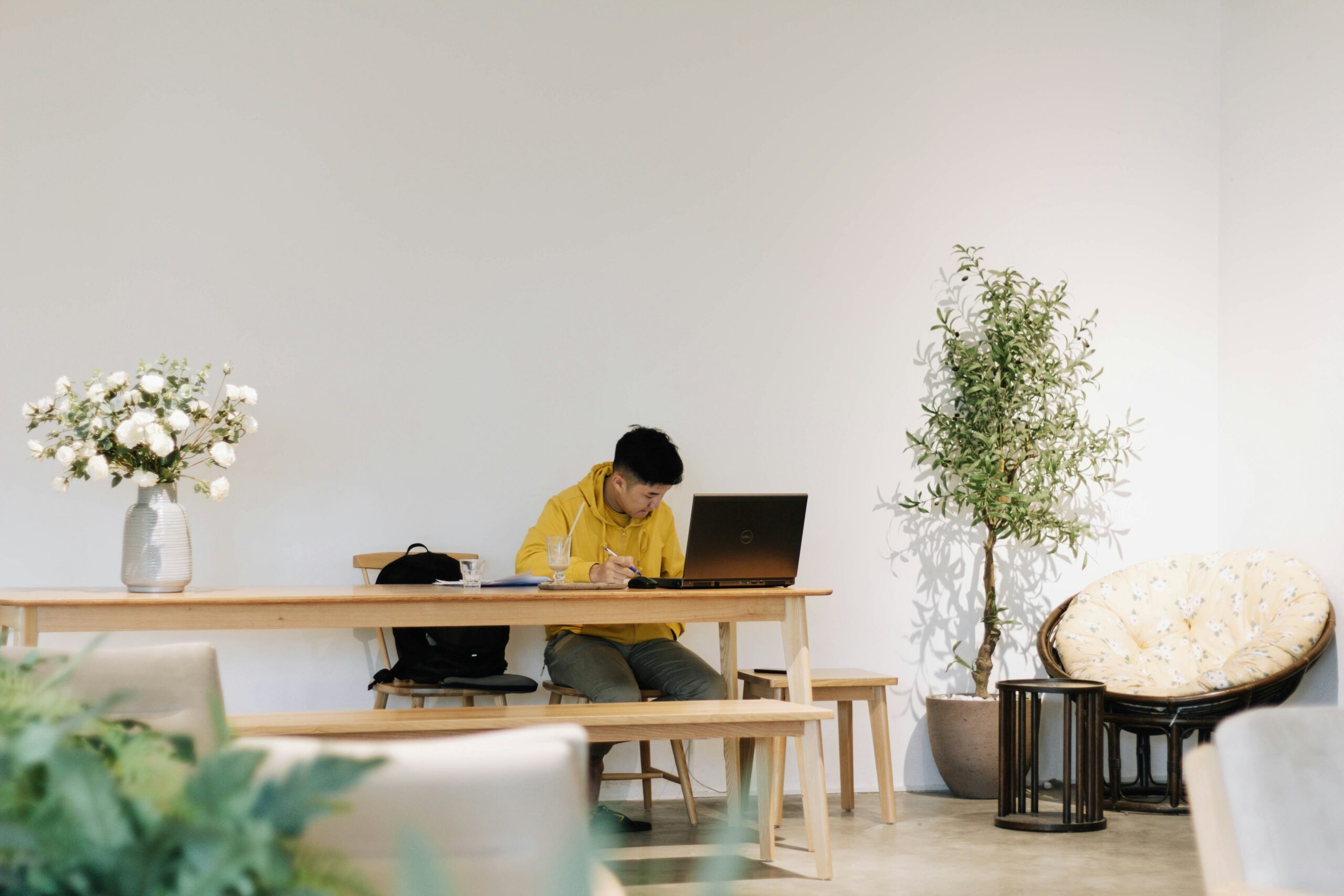 A man in a yellow jacket working on a laptop at a minimalistic café