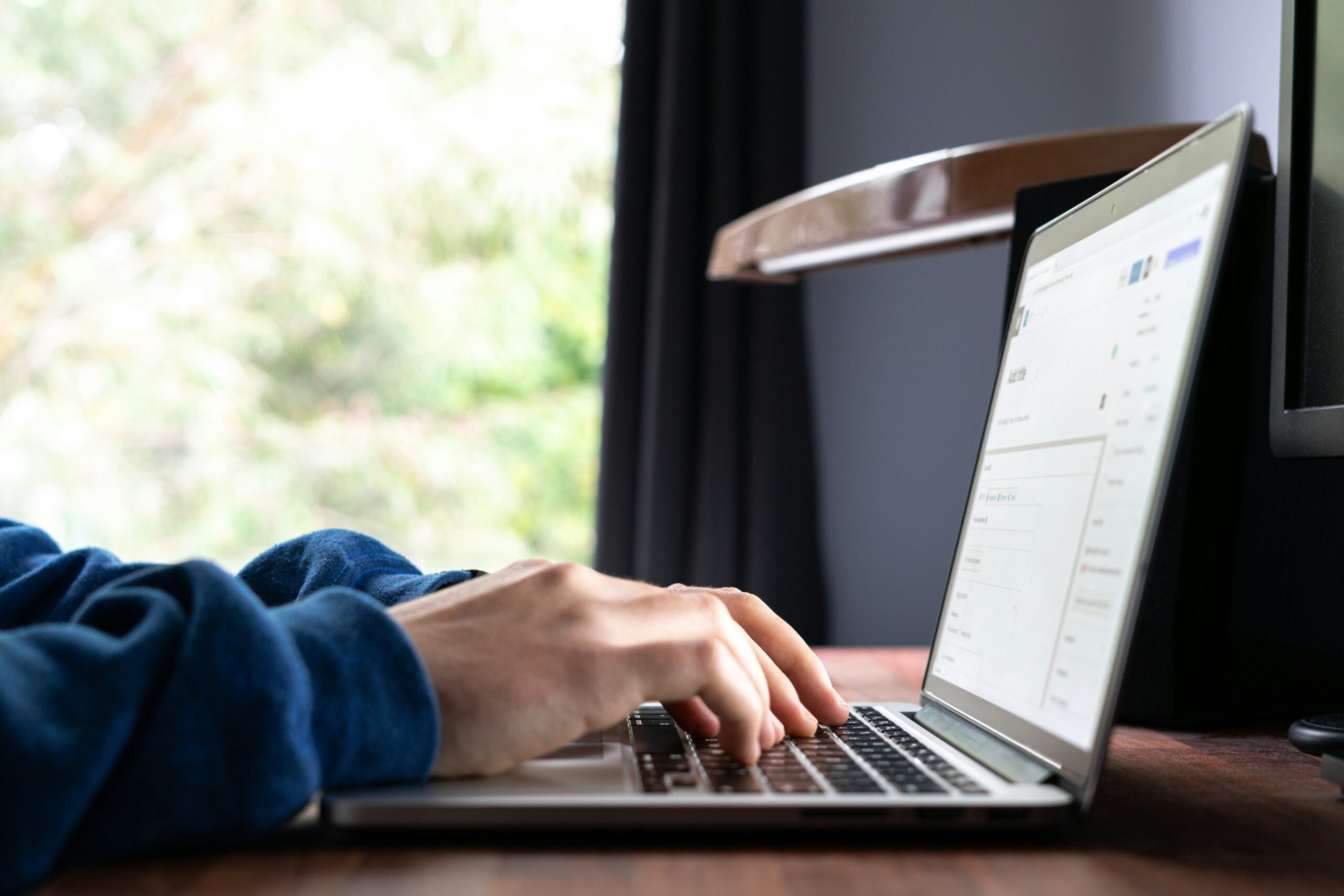 Person using a laptop at a desk with a blurred outdoor view, representing a comparison of AI writing tools.