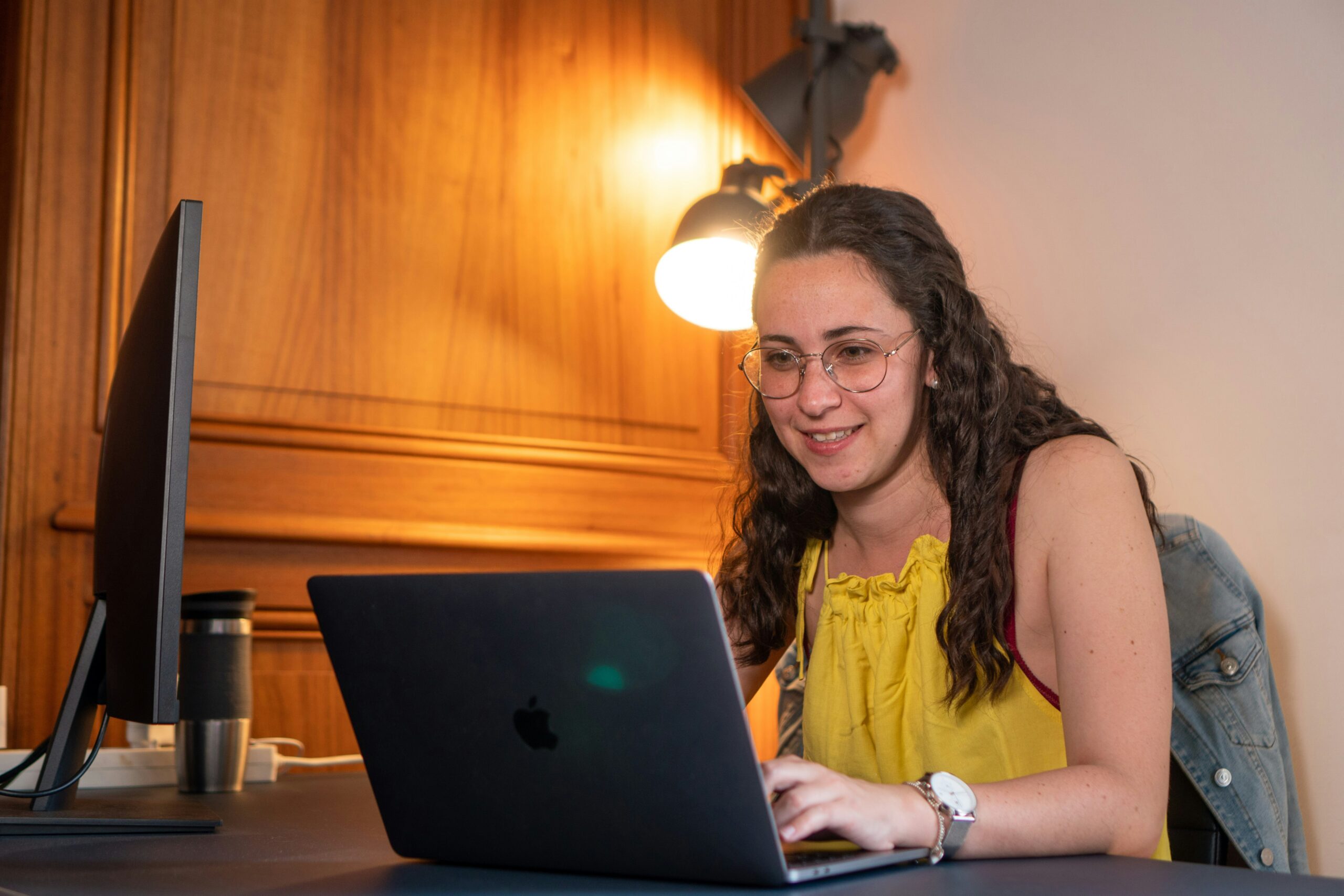 Woman smiling while working on a laptop in a warmly lit room