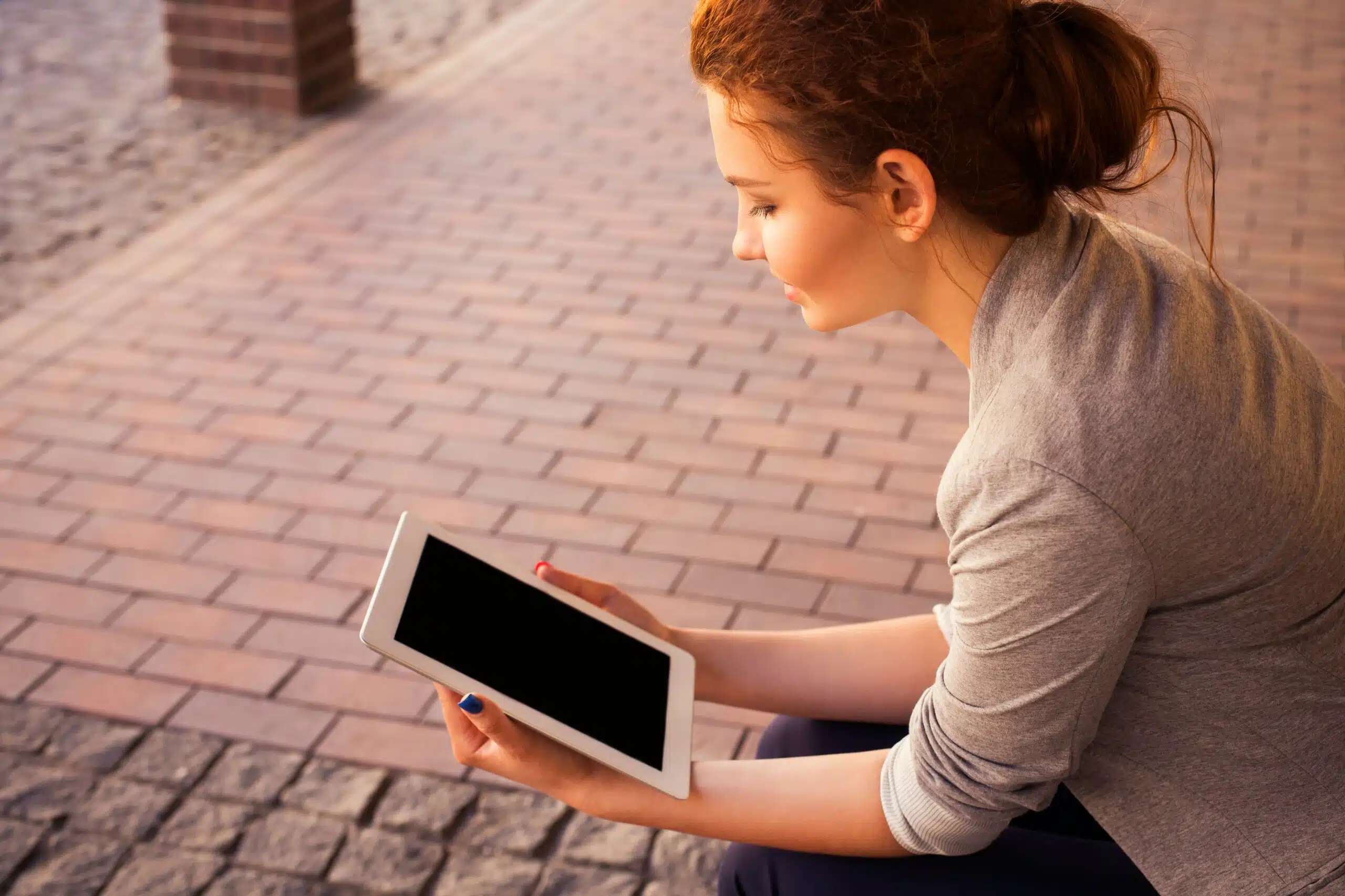 A woman sitting outdoors, examining AI-powered customer analytics on her tablet.