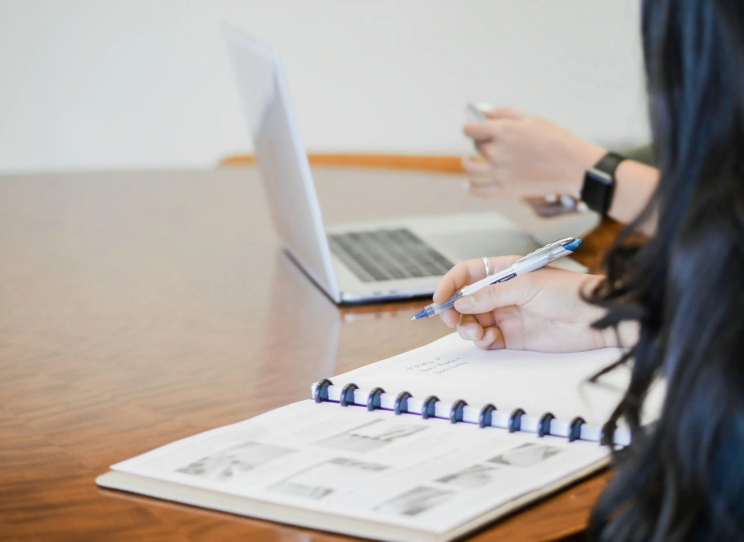 Close-up of a notebook and laptop as a professional takes notes on automated reporting