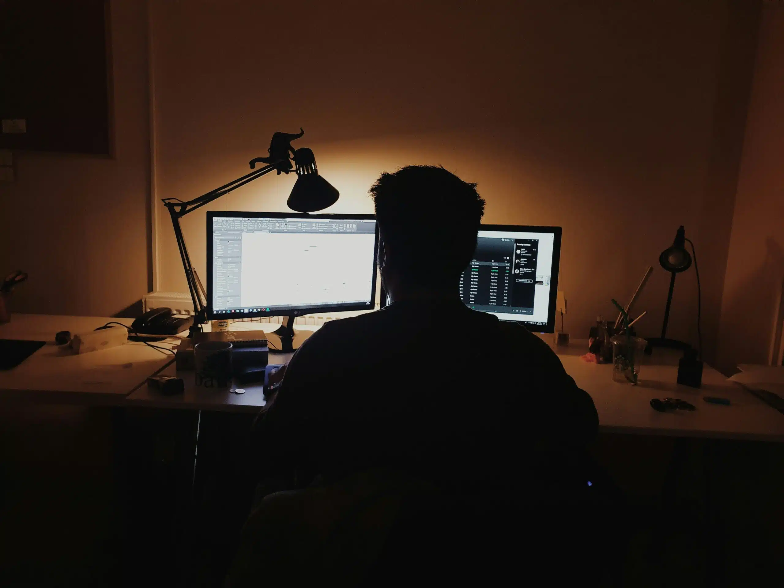  person working late at night on dual computer monitors