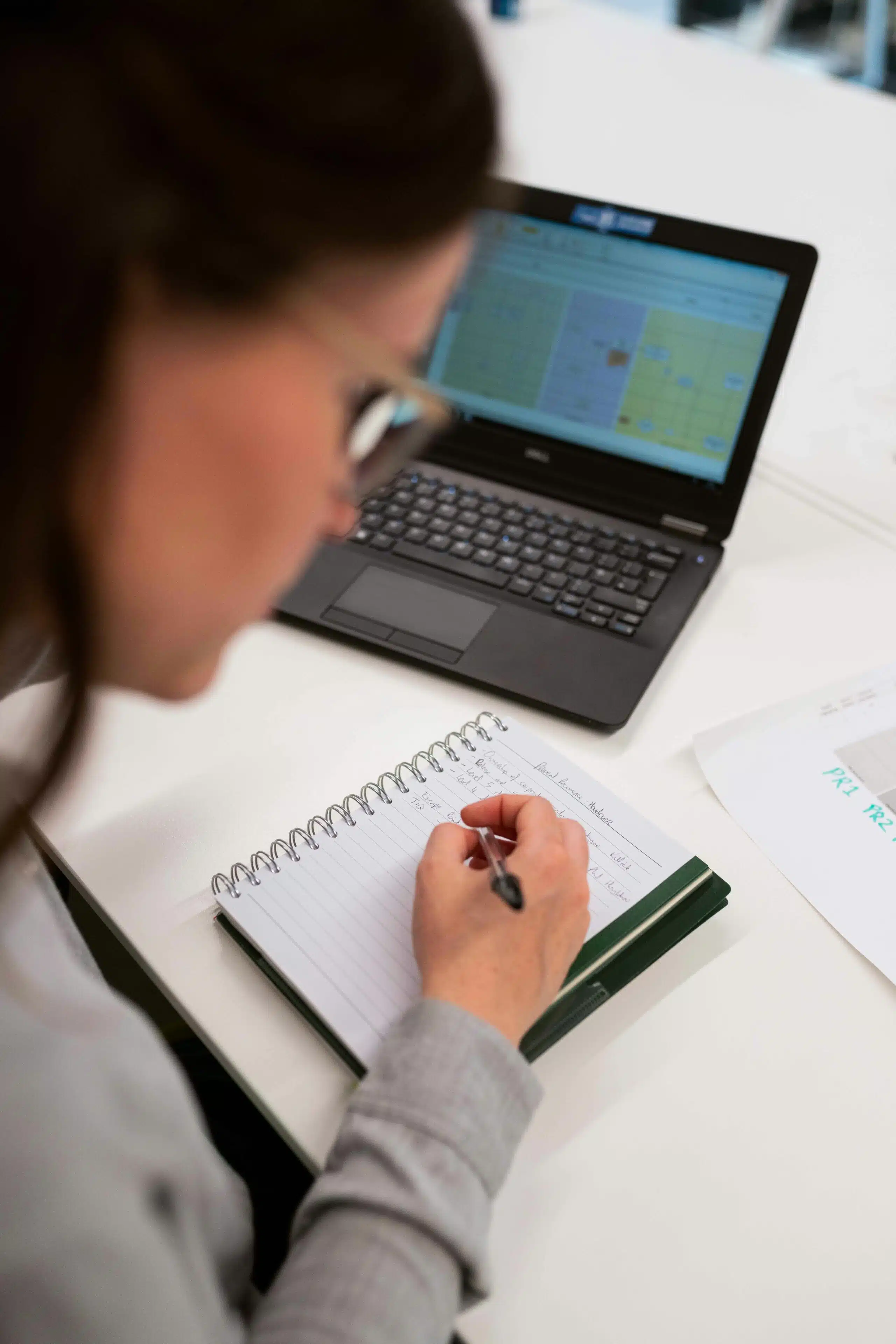 Professional taking notes while analyzing AI-generated data on laptop