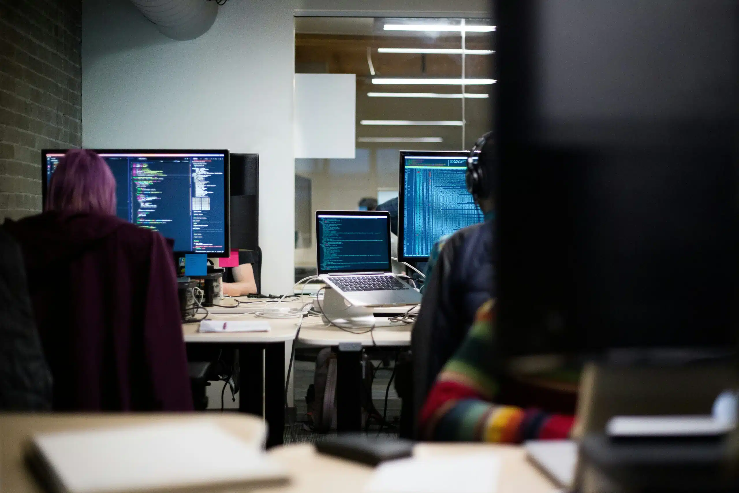 Developers coding at a shared workspace with multiple monitors displaying programming environments