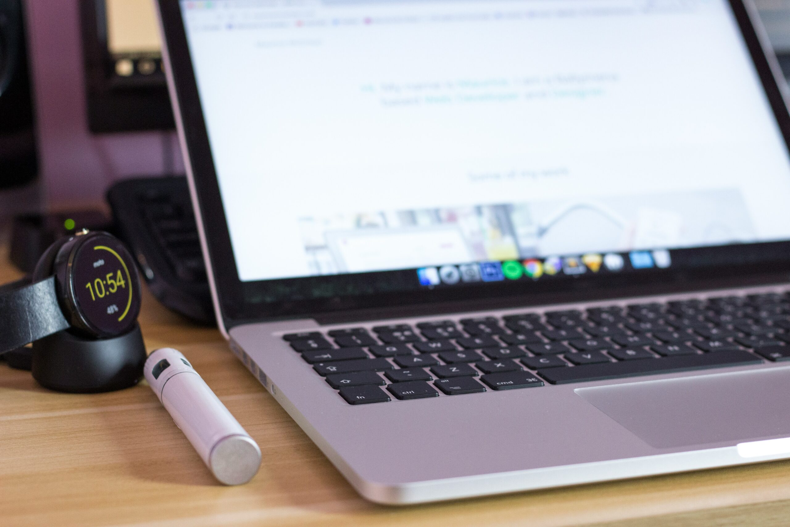 Close-up of a laptop with smartwatch and stylus on a wooden desk. - AI Marketing Tools Close-up of a laptop with smartwatch and stylus on a wooden desk.