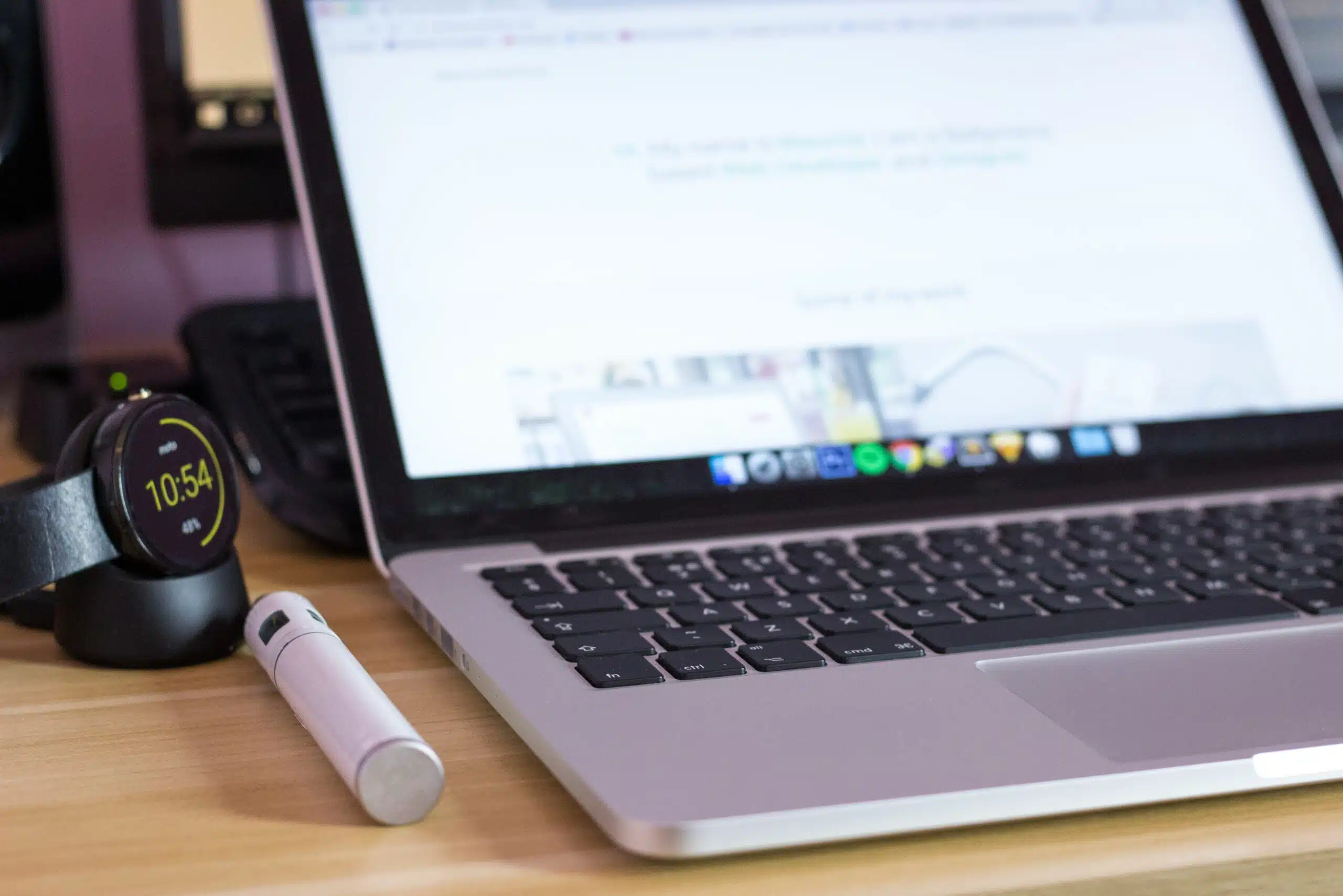 Close-up of a laptop with smartwatch and stylus on a wooden desk.