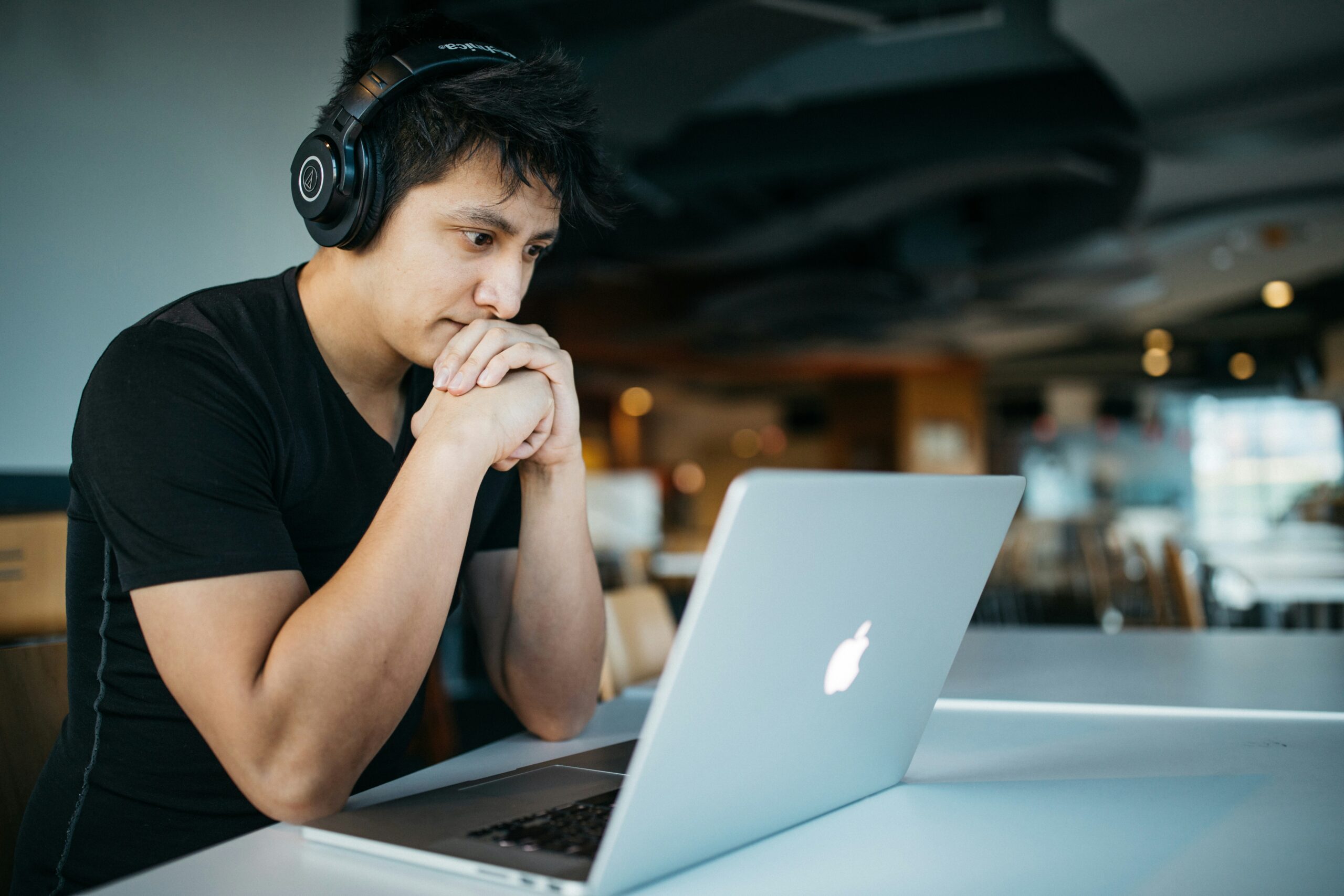 Focused man wearing headphones working on a MacBook - AI Marketing Tools Focused man wearing headphones working on a MacBook