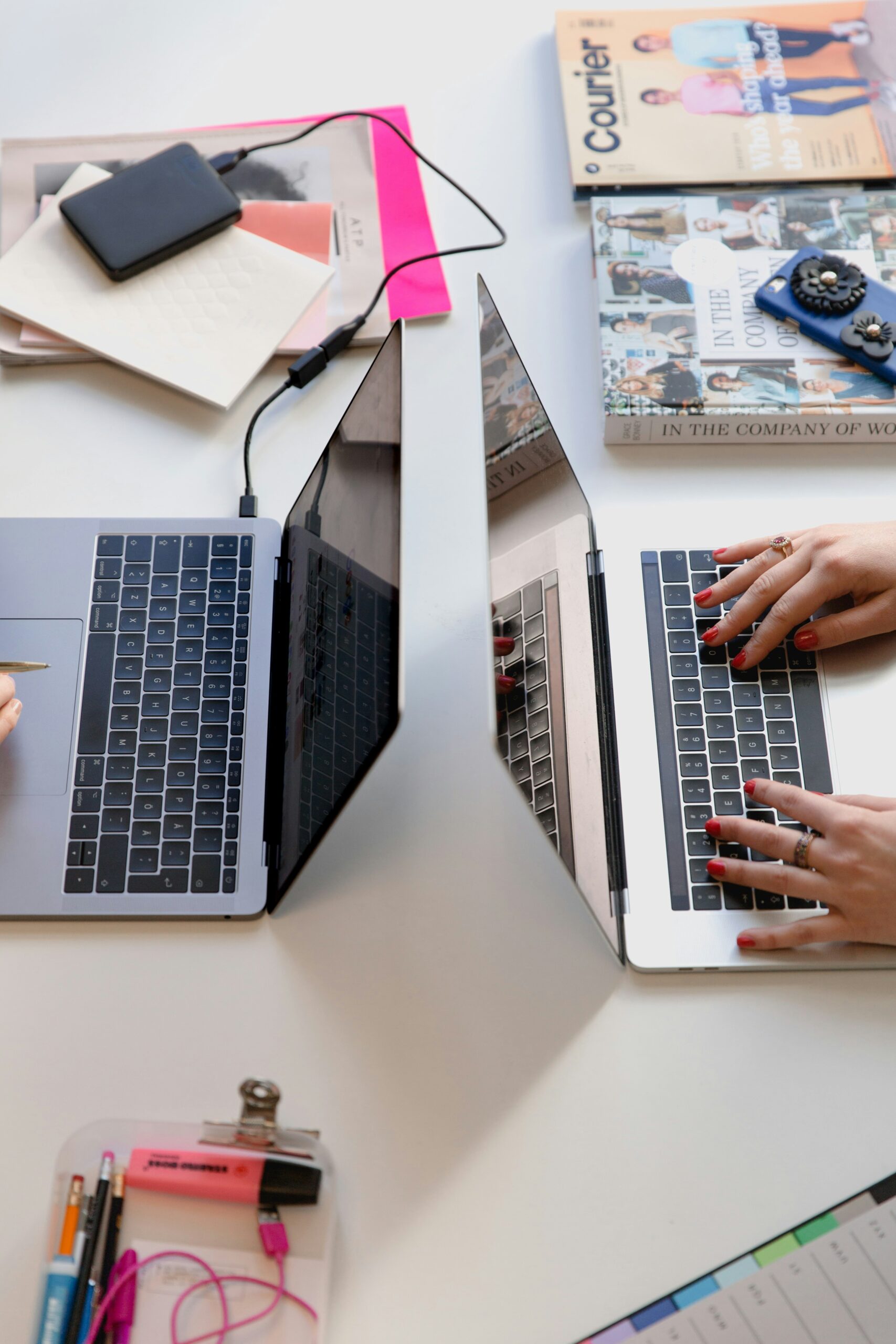 Two people working on laptops surrounded by books and notebooks on a shared desk. - AI Marketing Tools two laptops placed on a work desk