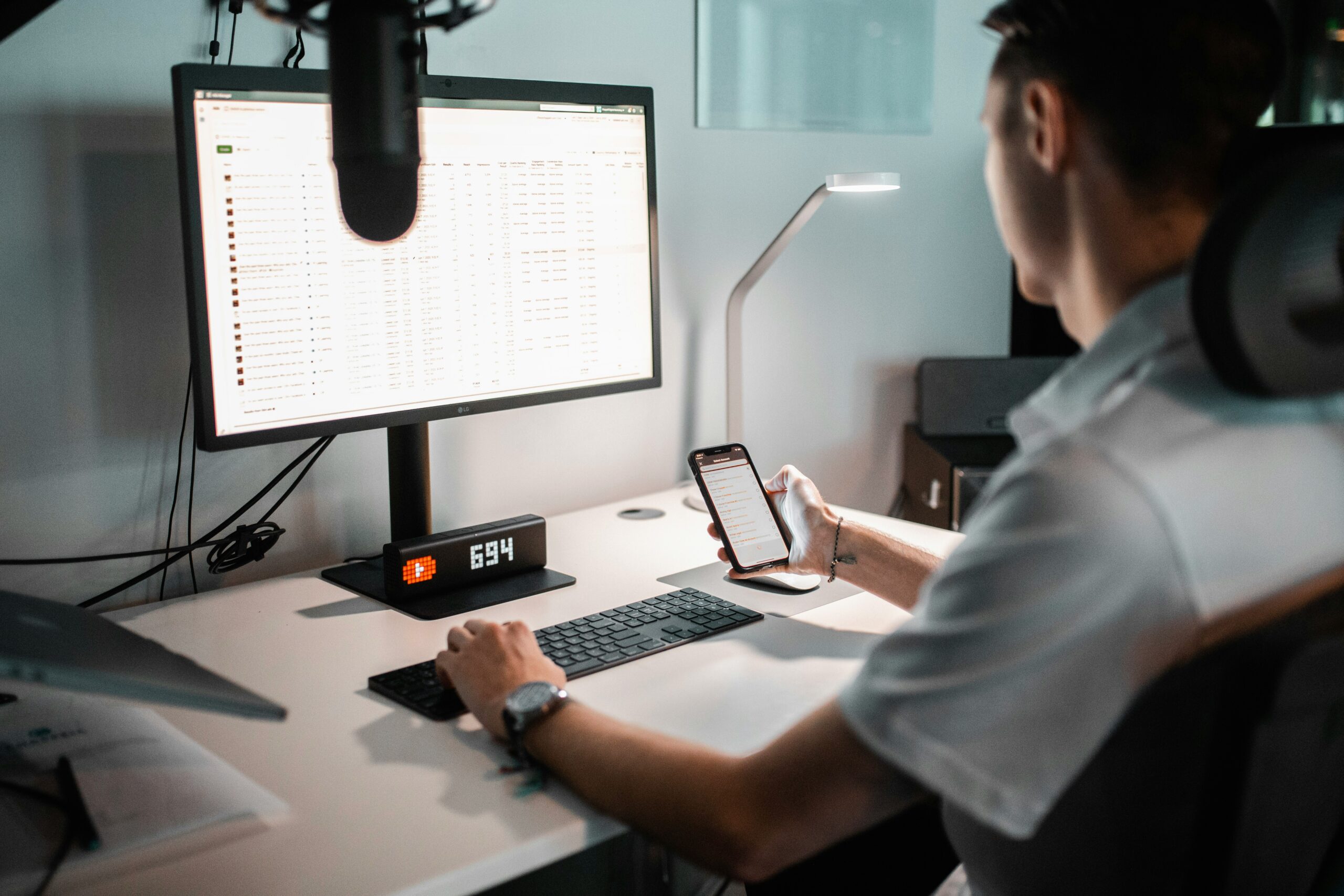 Man analyzing large datasets using a smartphone and desktop screen.